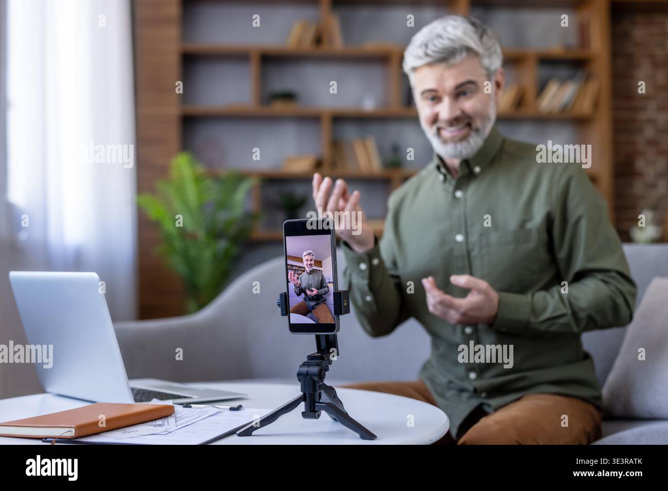 Uomo maturo che presenta e registra un video educativo con il suo smartphone su un treppiede, fornisce coaching online o partecipa a un webinar dal suo ufficio domestico Foto Stock