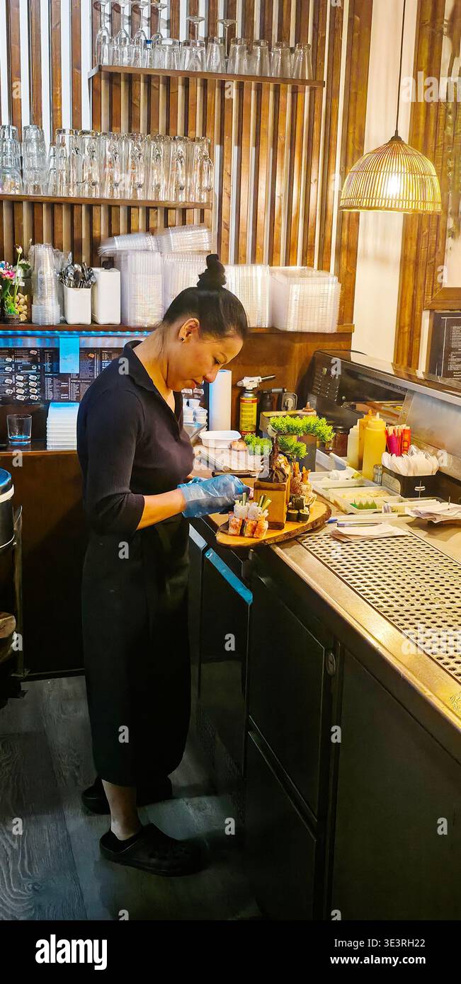 Berlino, Germania - 25 giugno 2025: Chef asiatica prepara sushi in una cucina moderna con ingredienti freschi al banco. - Immagine stock catturata con smartphone