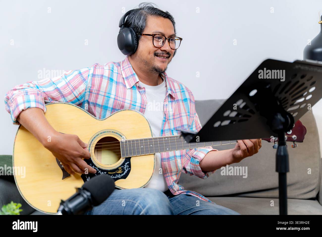 Un giovane riproduce in streaming le sue performance di chitarra da casa, rappresentando intrattenimento online, creatività musicale e creazione di contenuti digitali. Foto Stock
