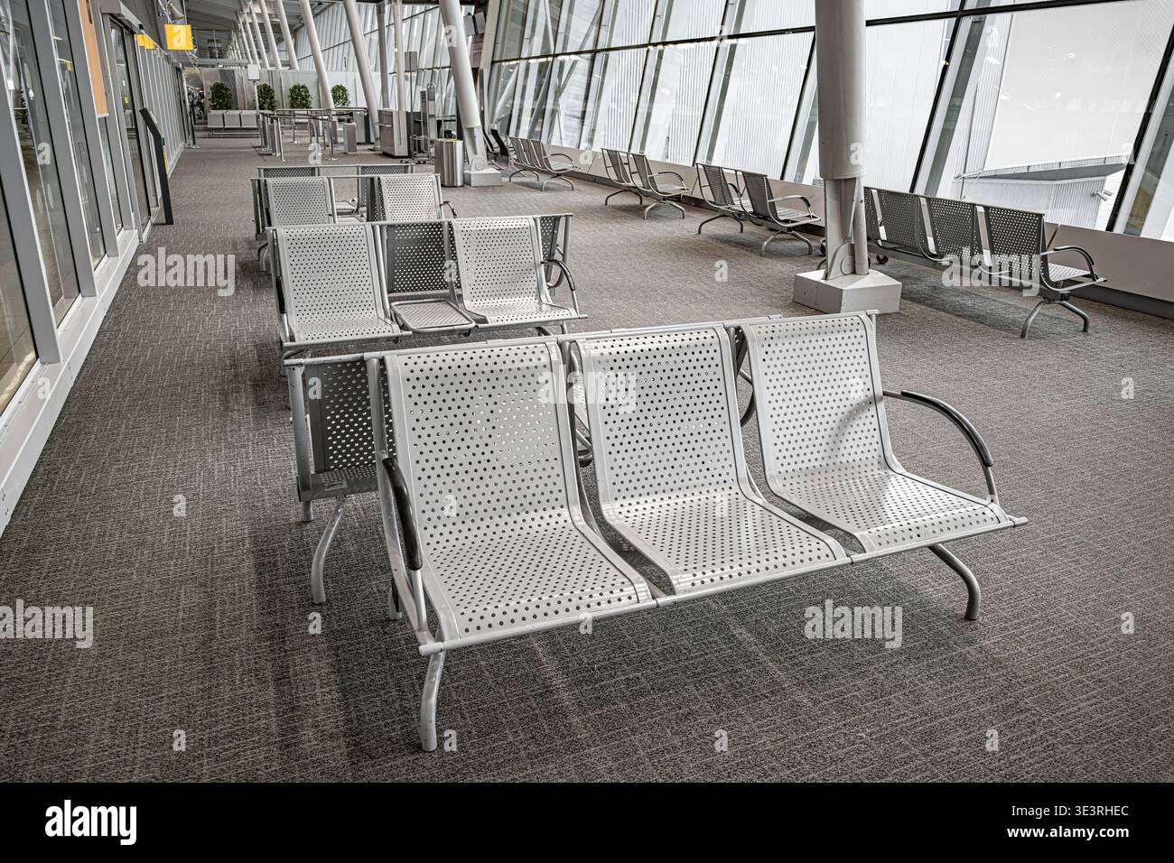 Una sala partenze vuota in un moderno terminal aeroportuale presenta file di posti a sedere in metallo perforato. Foto Stock