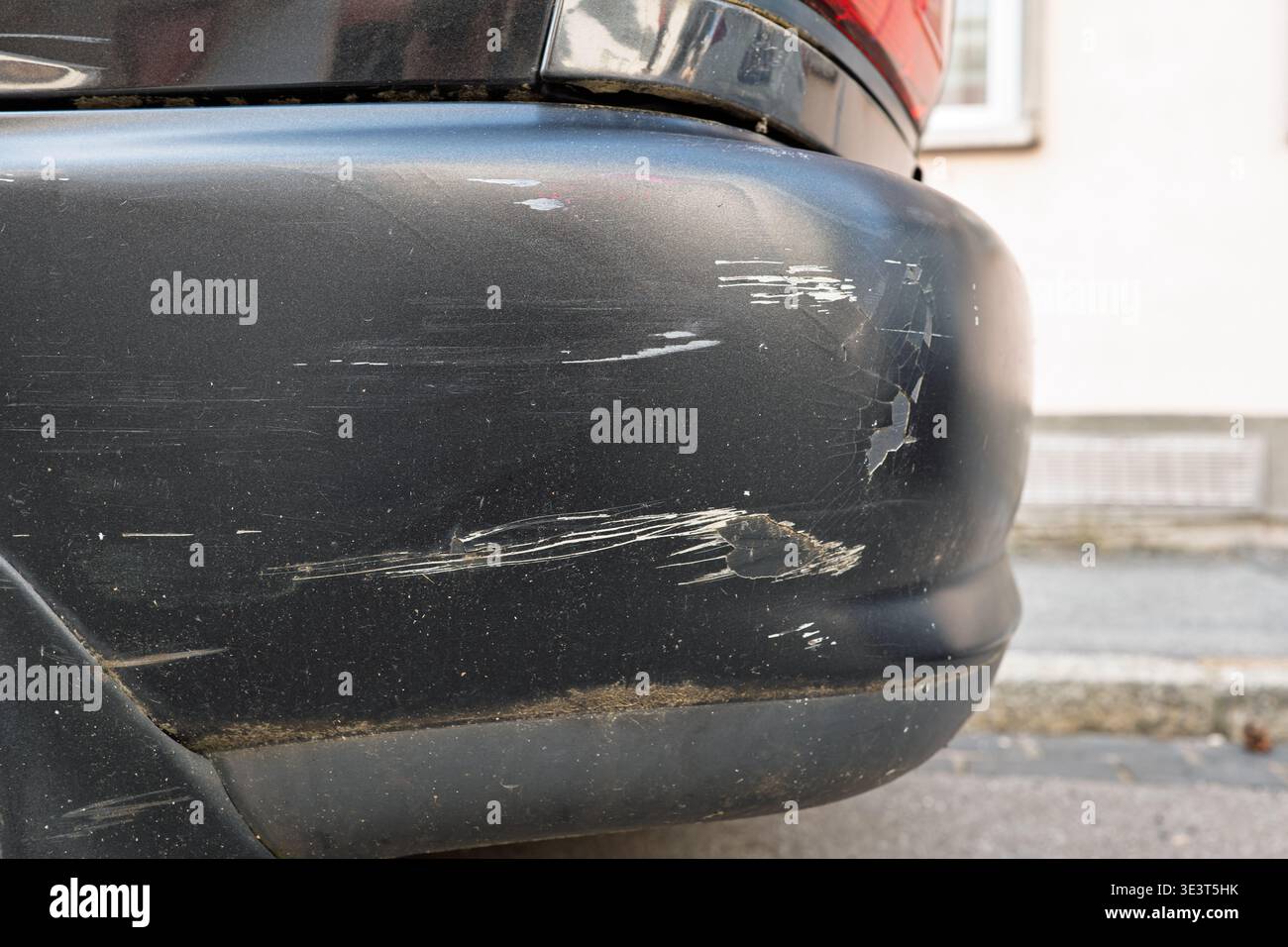 Vista dettagliata dei segni bianchi di rigatura e della vernice sbucciata sull'angolo del paraurti di un veicolo scuro dopo un incidente, che mostra la struttura danneggiata e l'impatto ma Foto Stock