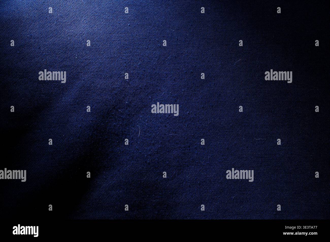 Foto macro di materiale tessile blu navy che mostra un motivo a trama dettagliata e luci soffuse sotto un'illuminazione a contrasto elevato per uno sfondo elegante. Foto Stock