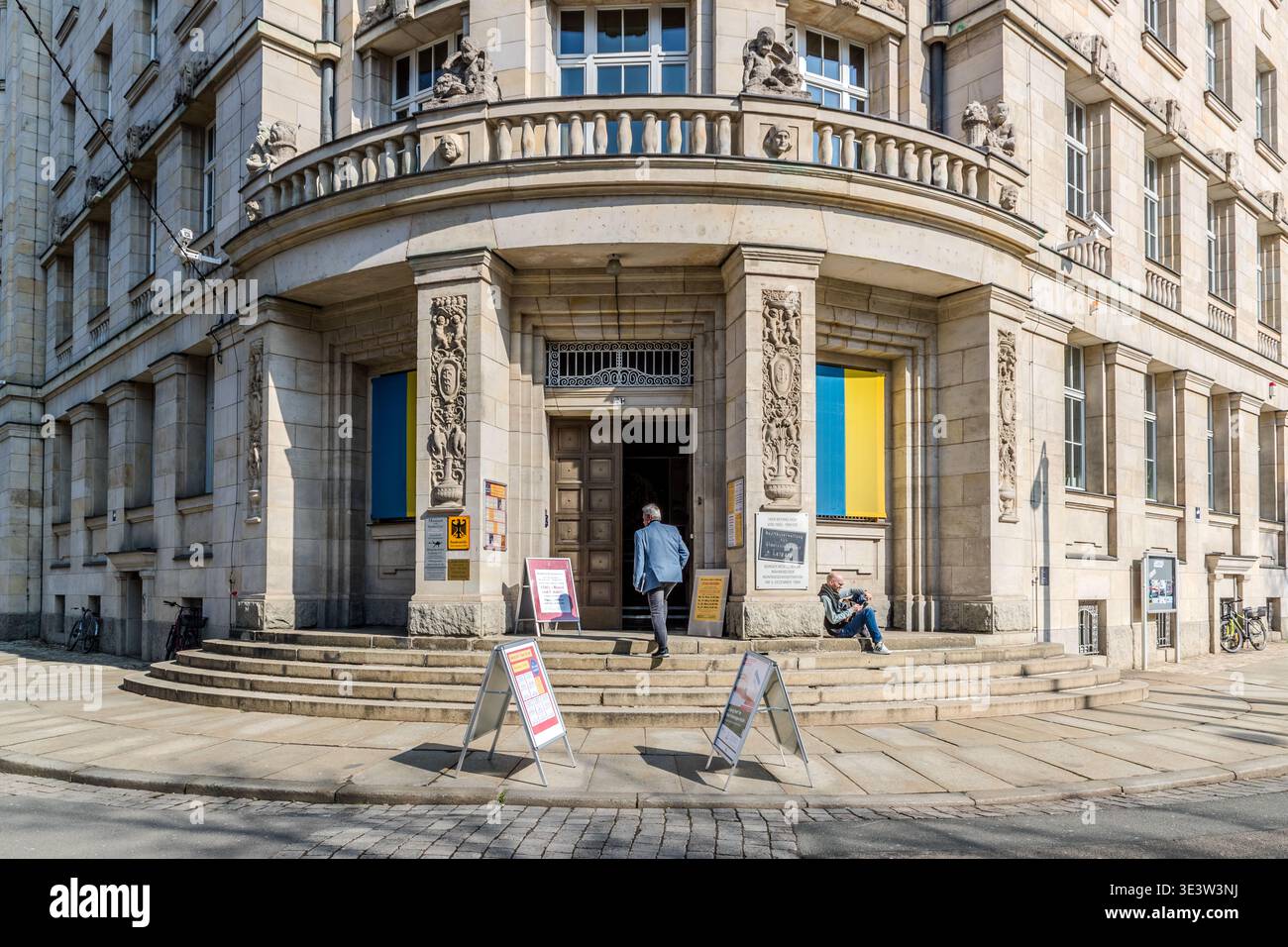 Il Runde Ecke era il quartier generale della Stasi a Lipsia. L'ingresso ad un maestoso edificio in stile Guglielmina nel centro di Lipsia, caratterizzato dall'aquila federale e dalle finestre incorniciate in giallo e blu (i colori ucraini, come simbolo di solidarietà); segnali di protesta in primo piano. Lipsia, Sassonia, Germania Foto Stock