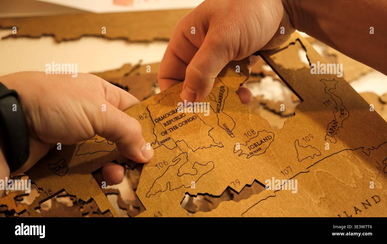 Le mani maschili estraggono un pezzo tagliato al laser da un foglio di compensato per assemblare una mappa del mondo decorativa in legno. Il processo creativo per creare oggetti fai da te Foto Stock