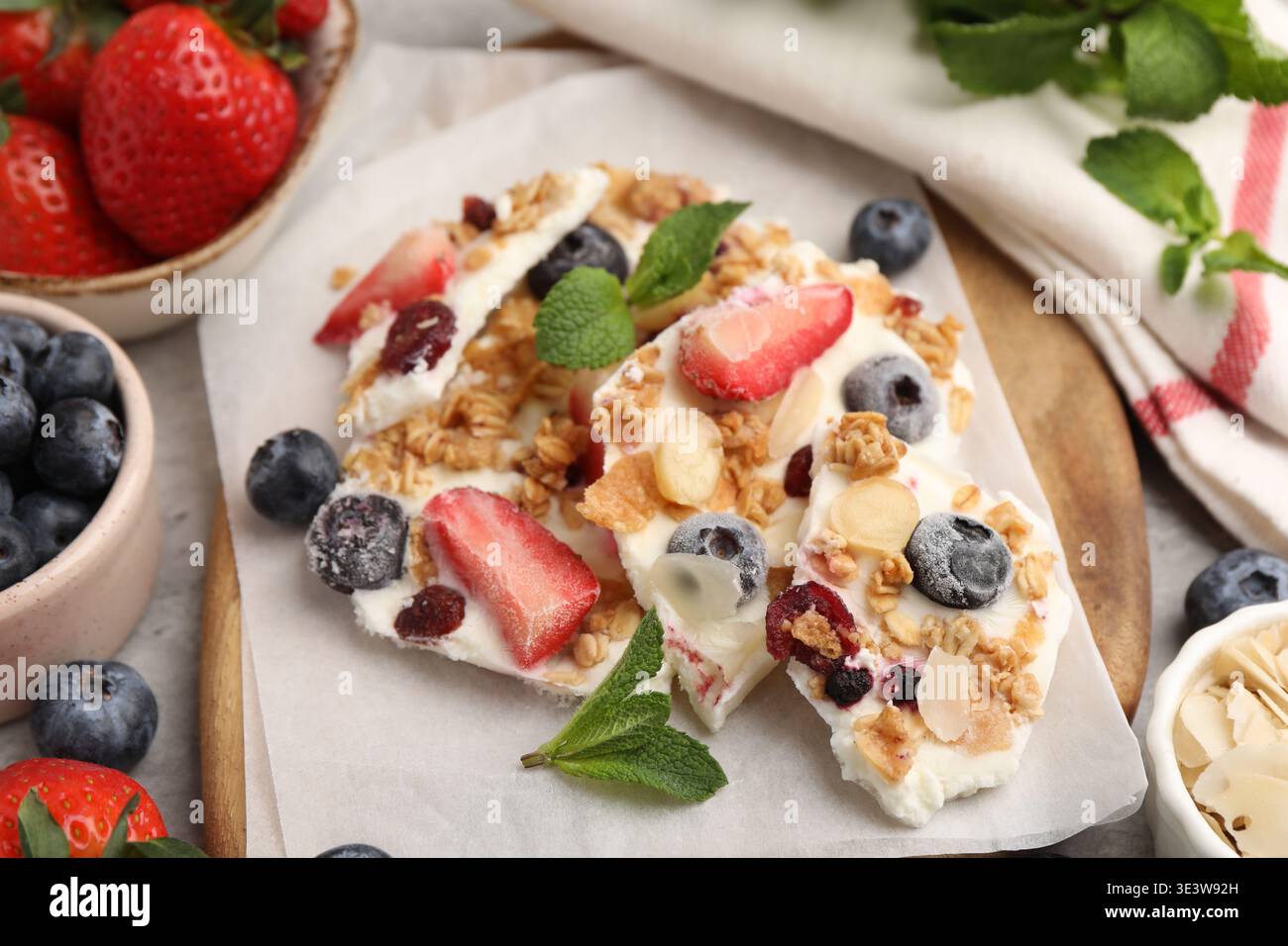 Pezzi di gustosa corteccia di yogurt con frutti di bosco, muesli, scaglie di mandorle e menta sul tavolo grigio, primo piano Foto Stock
