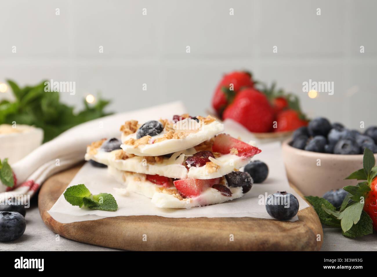 Pezzi di gustosa corteccia di yogurt con frutti di bosco, muesli e menta sul tavolo grigio, primo piano Foto Stock