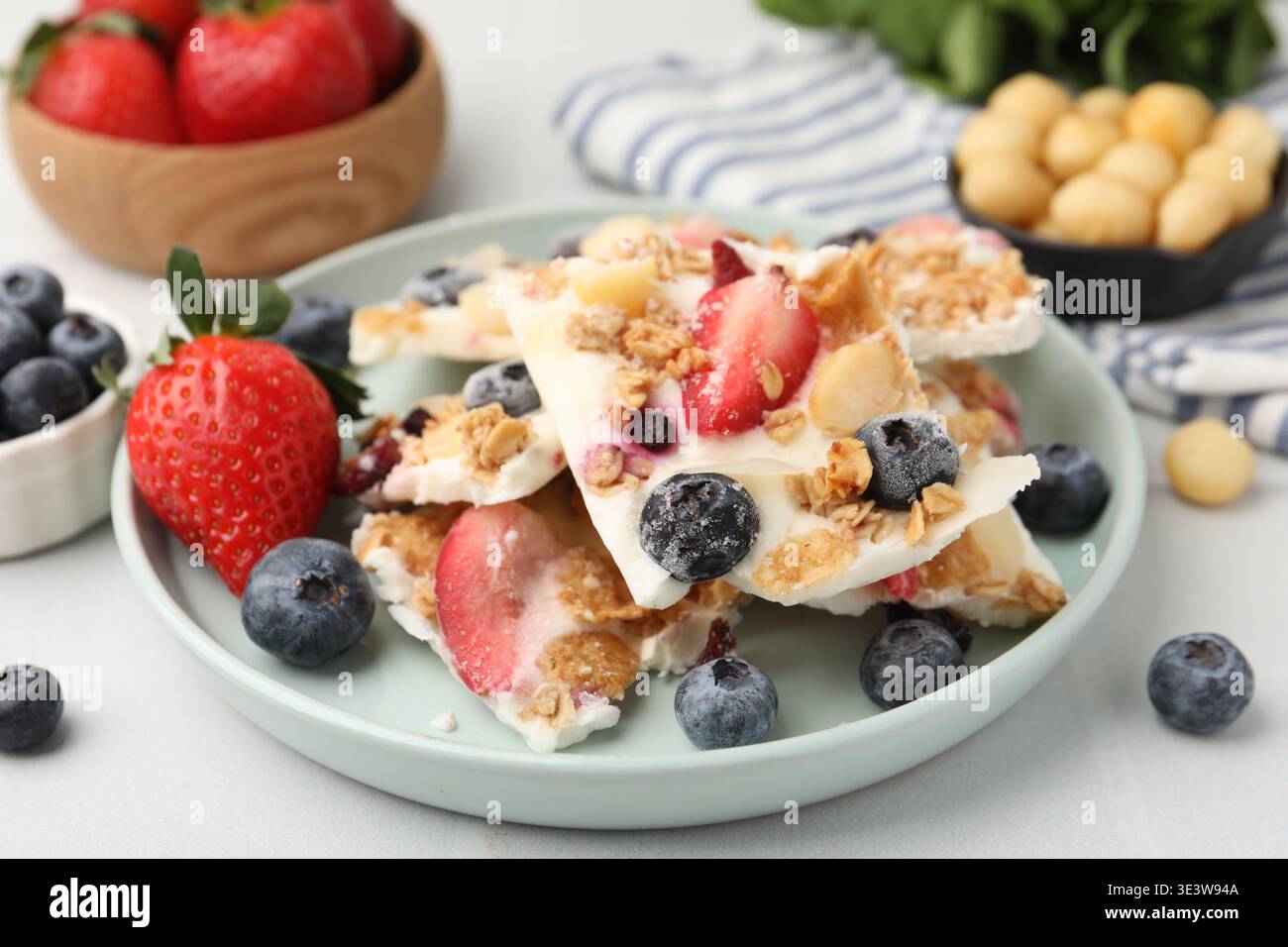 Pezzi di gustosa corteccia di yogurt con frutti di bosco e muesli sul tavolo leggero, primo piano Foto Stock