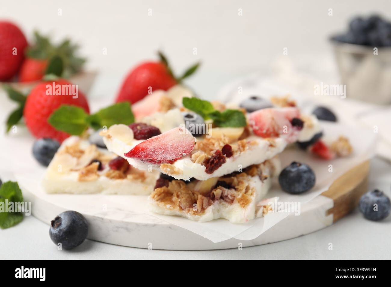 Pezzi di gustosa corteccia di yogurt con frutti di bosco, muesli e menta sul tavolo leggero, primo piano Foto Stock