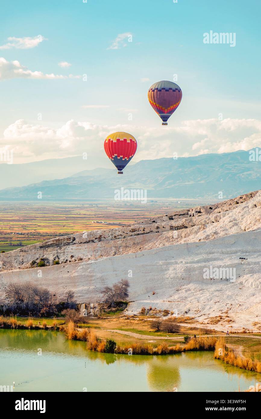 Due vibranti mongolfiere fluttuano graziosamente su uno splendido paesaggio naturale di colline ondulate e un tranquillo lago, con uno sfondo di lontane montagne Foto Stock