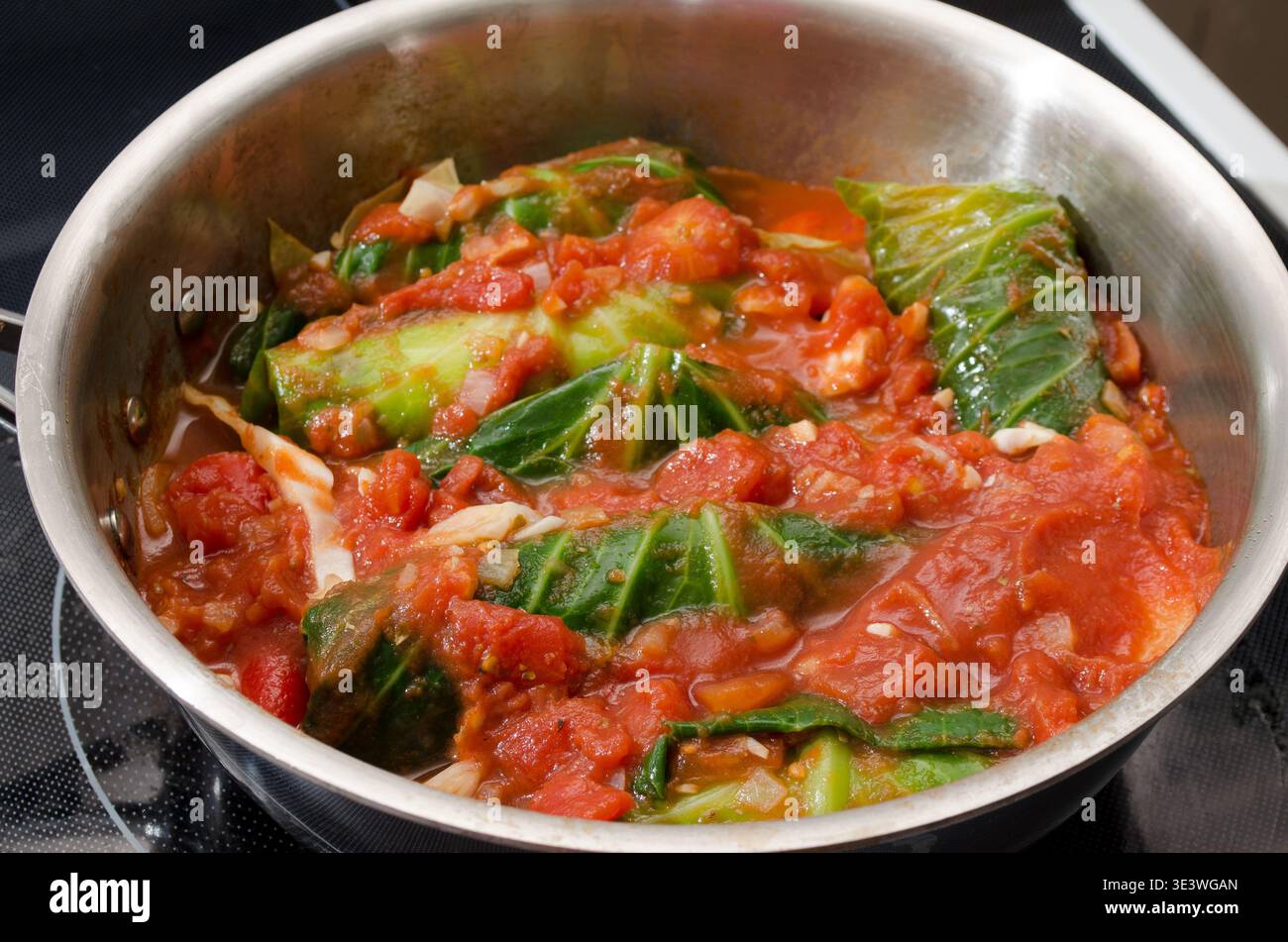 I rotoli di cavolo vengono sospesi in una ricca salsa di pomodoro in una padella in acciaio inossidabile. Il verde vibrante del cavolo è completato dal rosso della salsa. Foto Stock