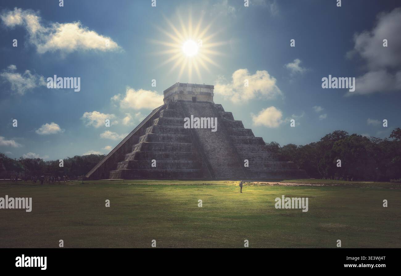 La maestosa piramide di Kukulkan a Chichen Itza si erge sotto il sole radioso, gettando lunghe ombre attraverso la distesa erbosa, con uno sfondo di un vi Foto Stock