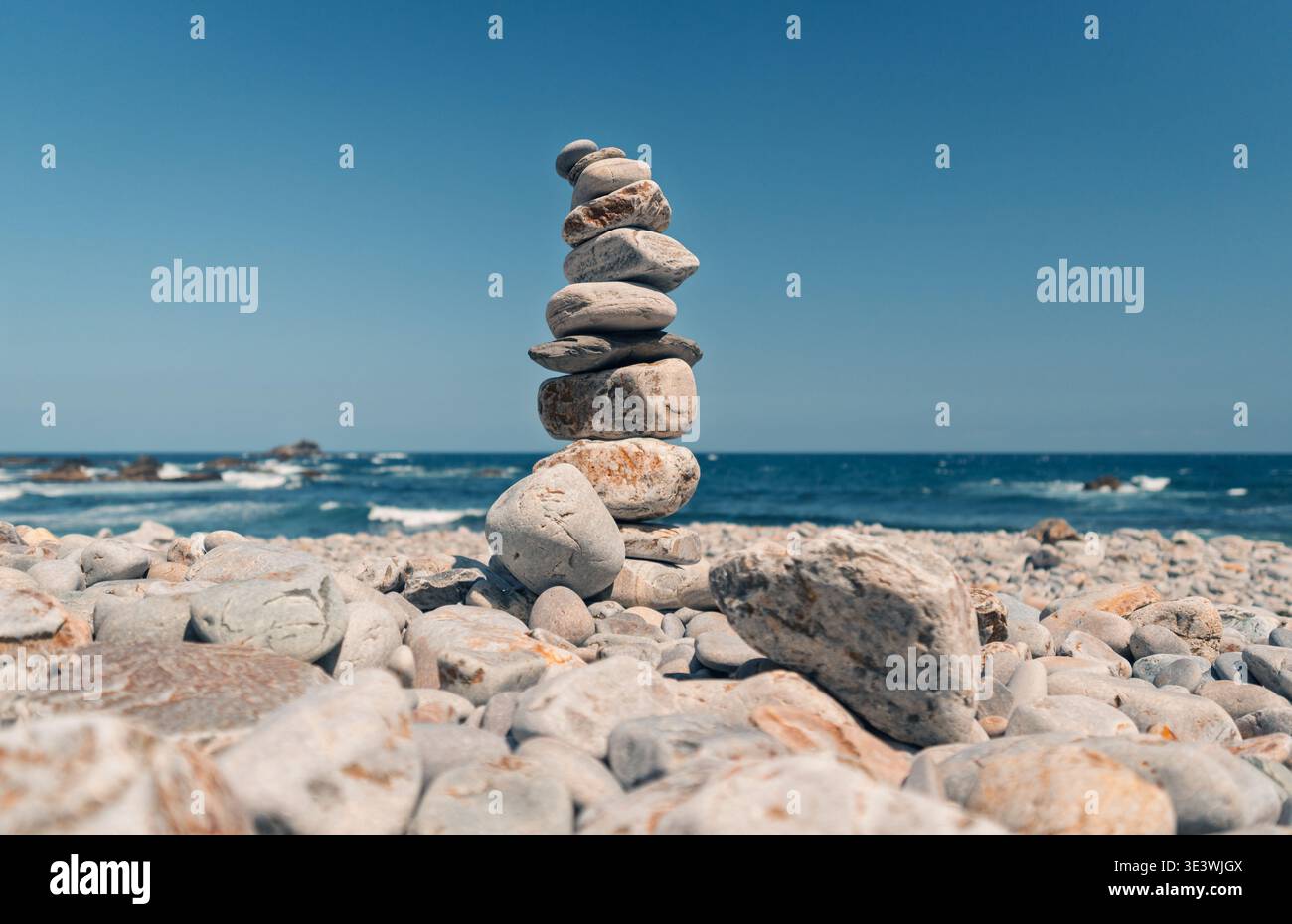Una pila di pietre lisce e intemperie è delicatamente bilanciata sulla costa rocciosa della spiaggia di Campiechos nelle Asturie, con l'oceano blu profondo e il cielo limpido Foto Stock