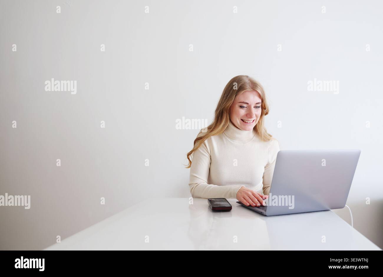 Giovane donna che usa un notebook alla scrivania. Lavoro freelance, comunicazione e produttività in un moderno ufficio domestico. Foto Stock