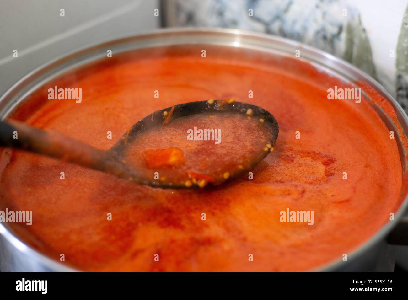 Cucchiaio mescolando la zuppa di pomodoro rosso spessa in una pentola, vista ravvicinata. Foto Stock