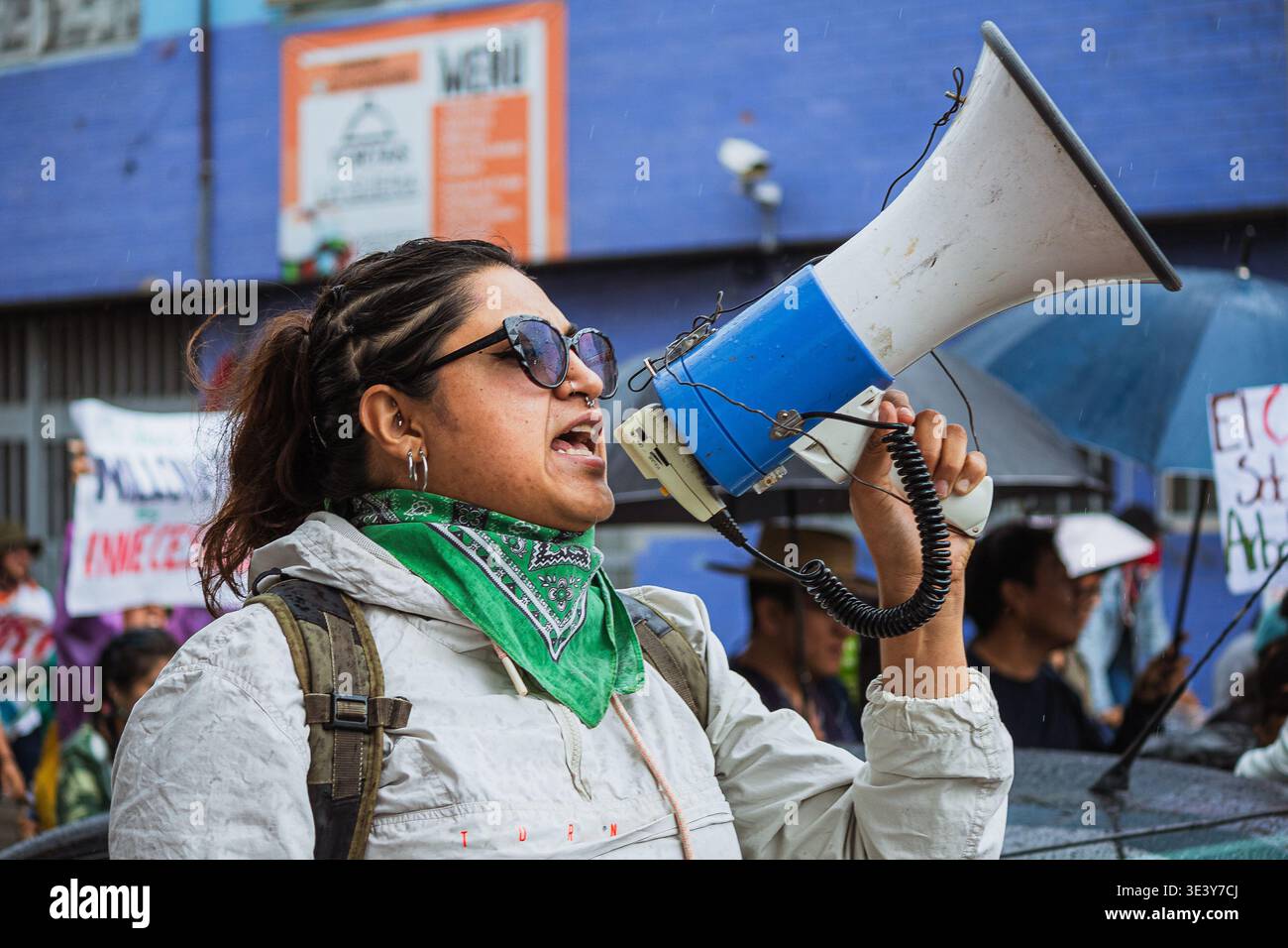 Una donna che indossa una bandana verde usa un megafono per condurre una protesta ambientale, chiedendo giustizia sociale e climatica all'aperto. Foto Stock