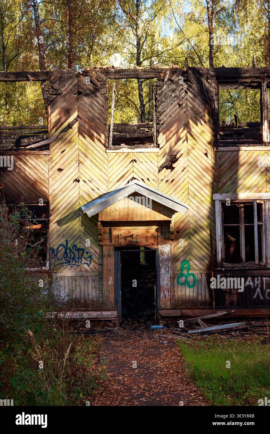 La casa in legno fatiscente e devastata dal fuoco si erge abbandonata in mezzo al fogliame autunnale. Questa rovina dimenticata, una testimonianza del tempo e della tragedia, recupera lentamente b Foto Stock
