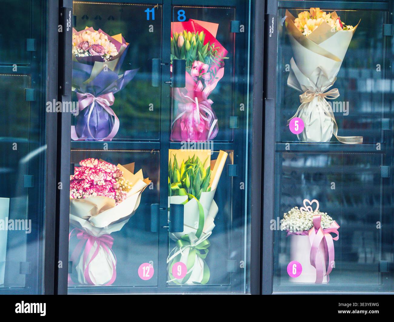 Fiori disposti in vetrine. Ciascun bouquet avvolto in carta o legato con nastro. I colori brillanti contrastano con lo sfondo scuro. Petali vivaci Foto Stock