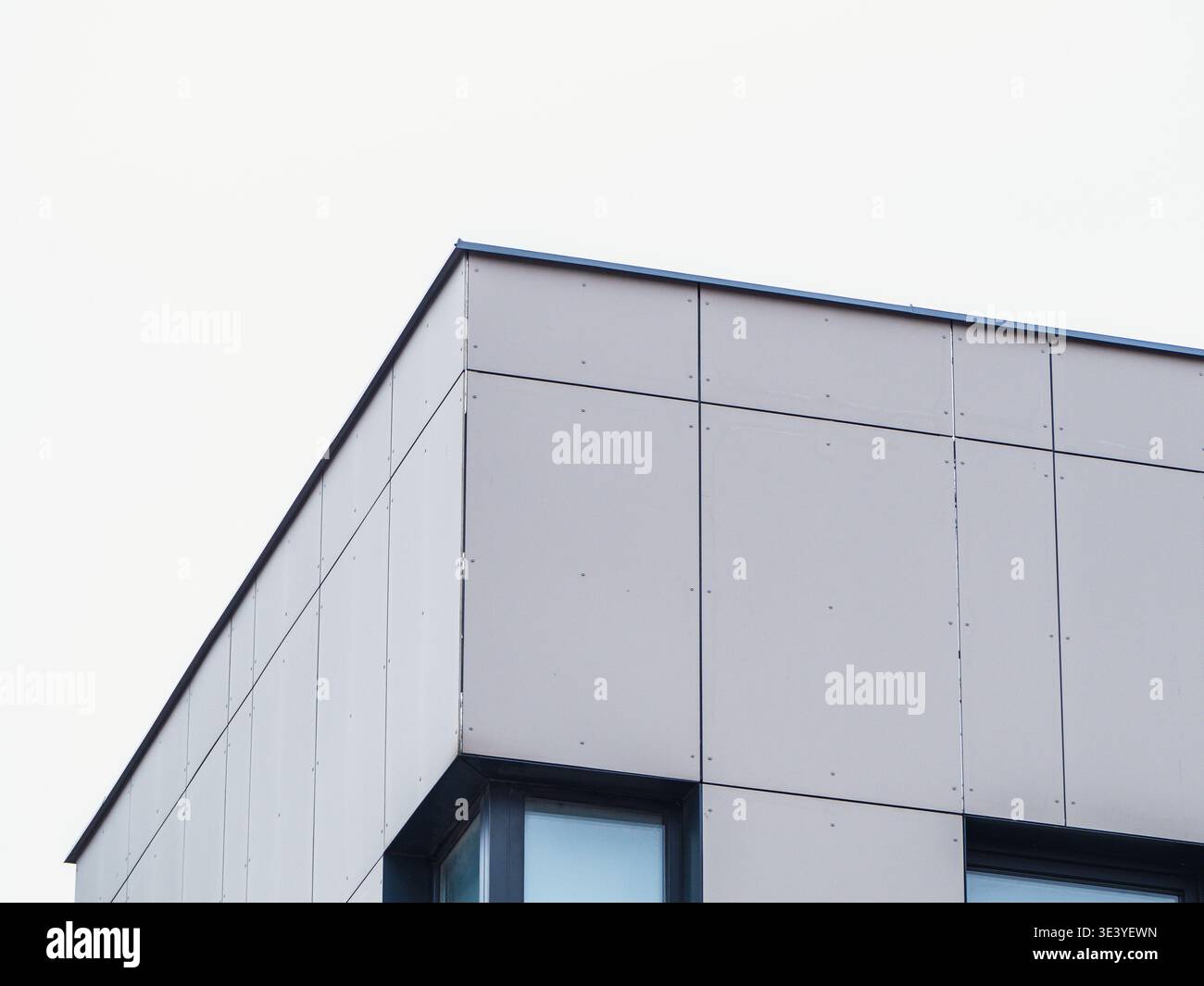 Edificio moderno con un design pulito e minimalista. I pannelli in grigio chiaro creano un motivo geometrico strutturato. Le finestre con cornice scura contrastano con quella liscia Foto Stock