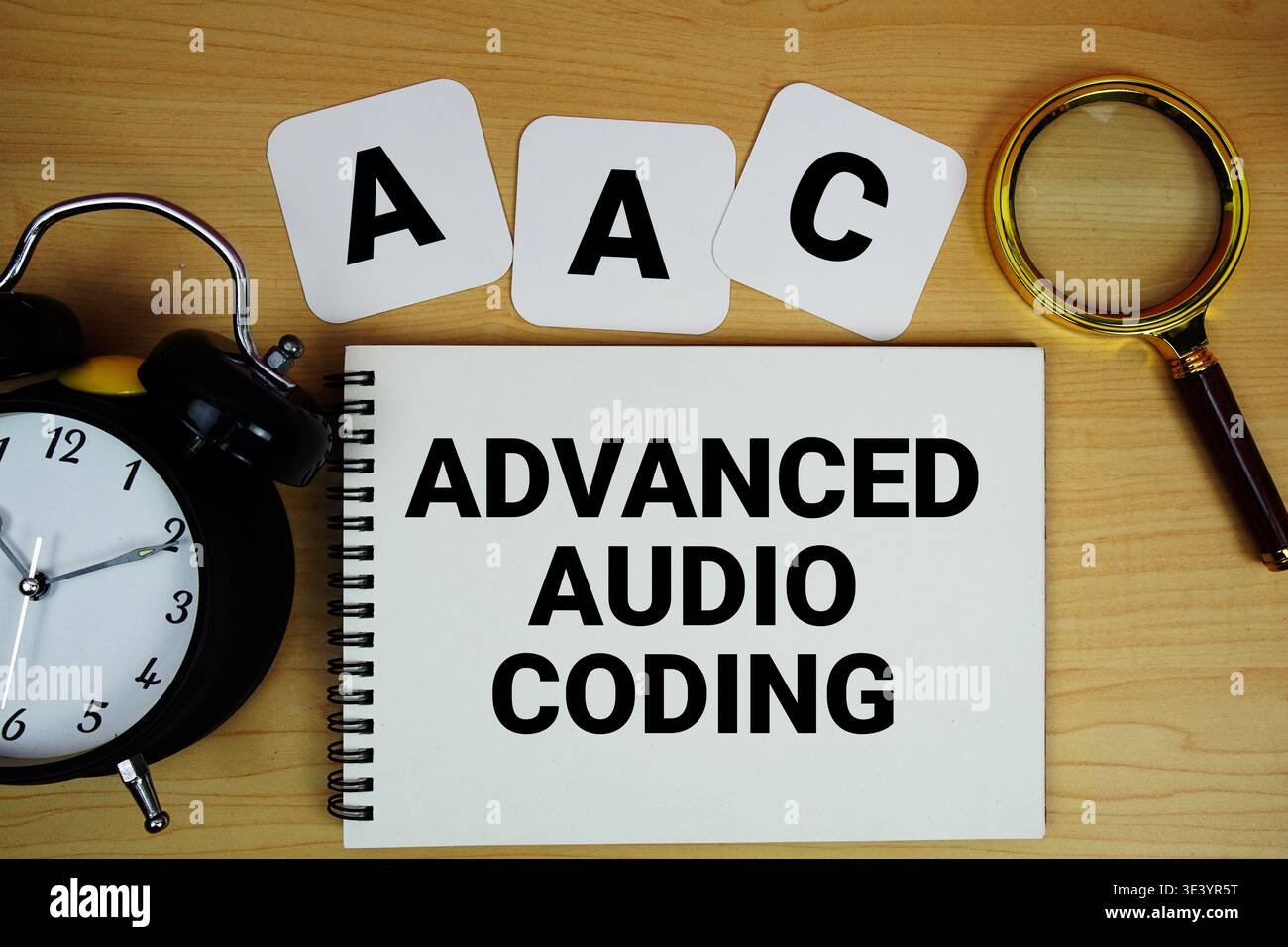 Testo AAC Advanced audio Coding scritto su blocco note con lente d'ingrandimento e sveglia su sfondo in legno Foto Stock