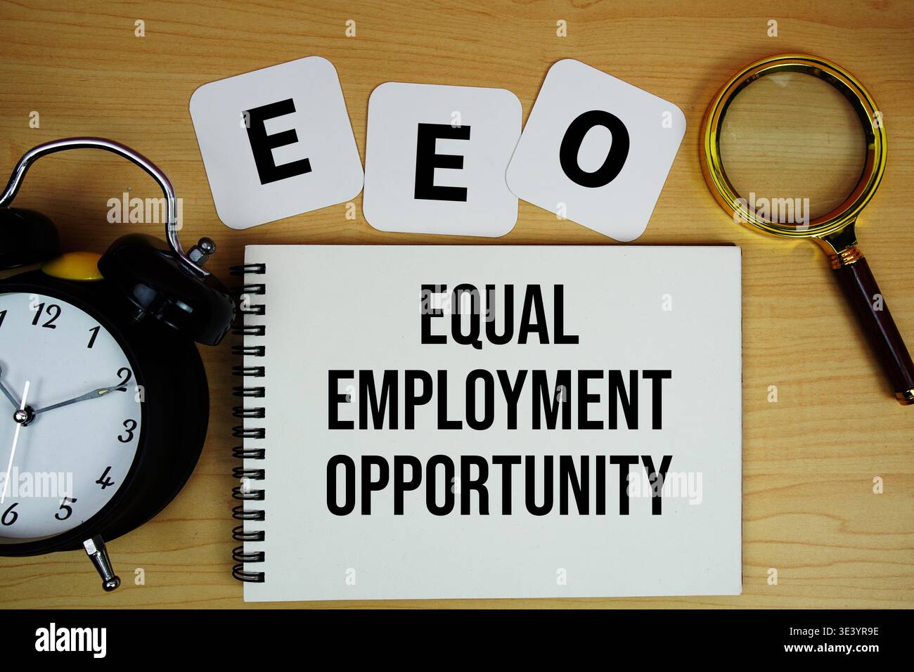 EEO Equal Employment Opportunity testo scritto su blocco note con lente d'ingrandimento e sveglia su sfondo in legno Foto Stock
