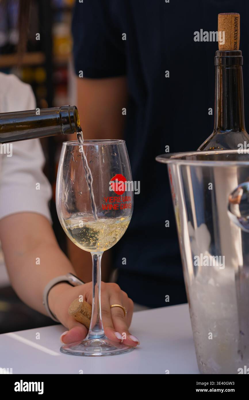 Al festival Yerevan Wine Days il vino bianco viene versato in un bicchiere di degustazione di marca da una bottiglia Foto Stock
