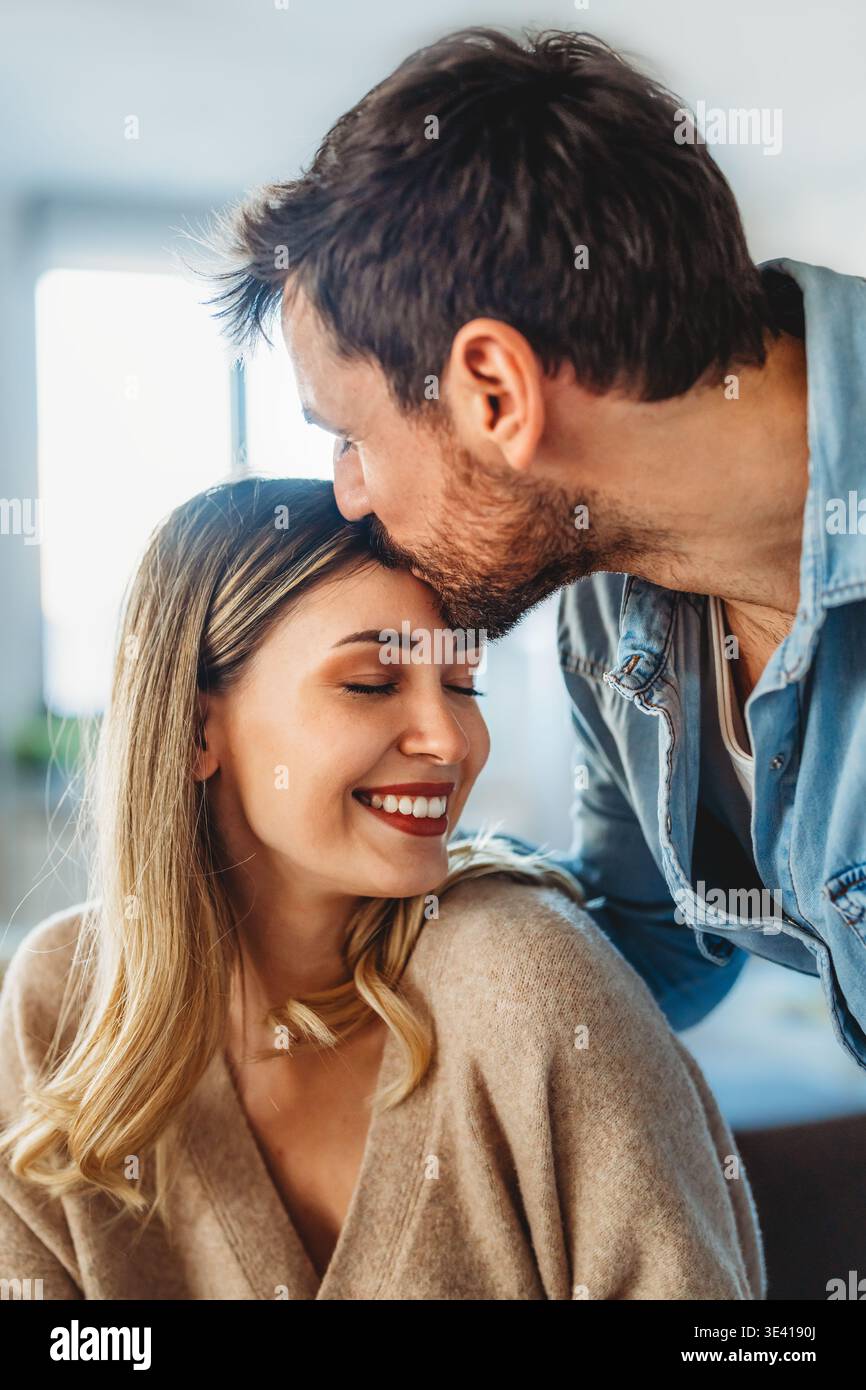 Coppia felice e variegata che condivide un momento di gioia a casa, abbracciando e sorridendo insieme Foto Stock