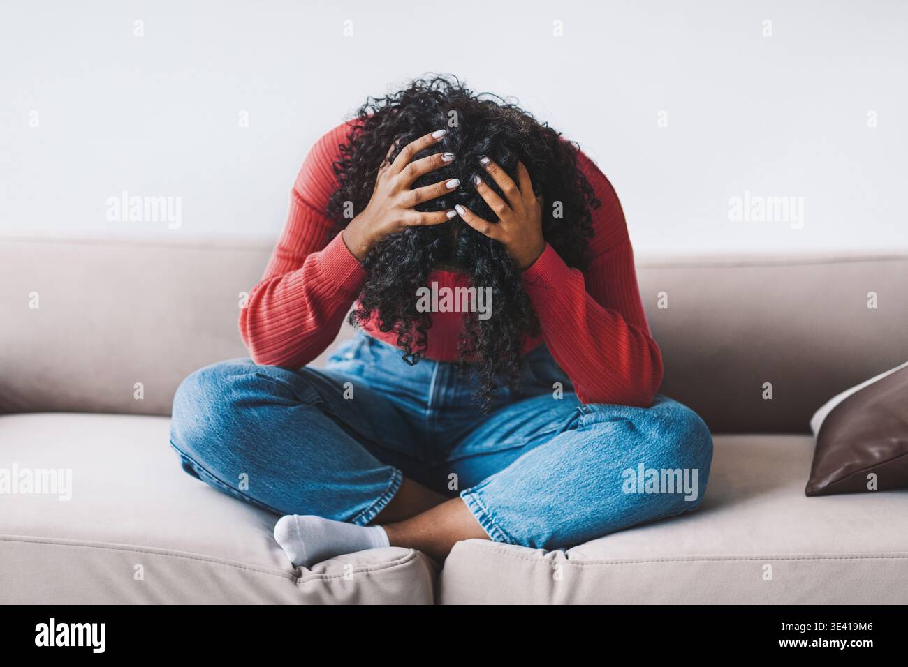 Donna seduta sul divano con la testa in mano che mostra sentimenti di stress durante il giorno Foto Stock