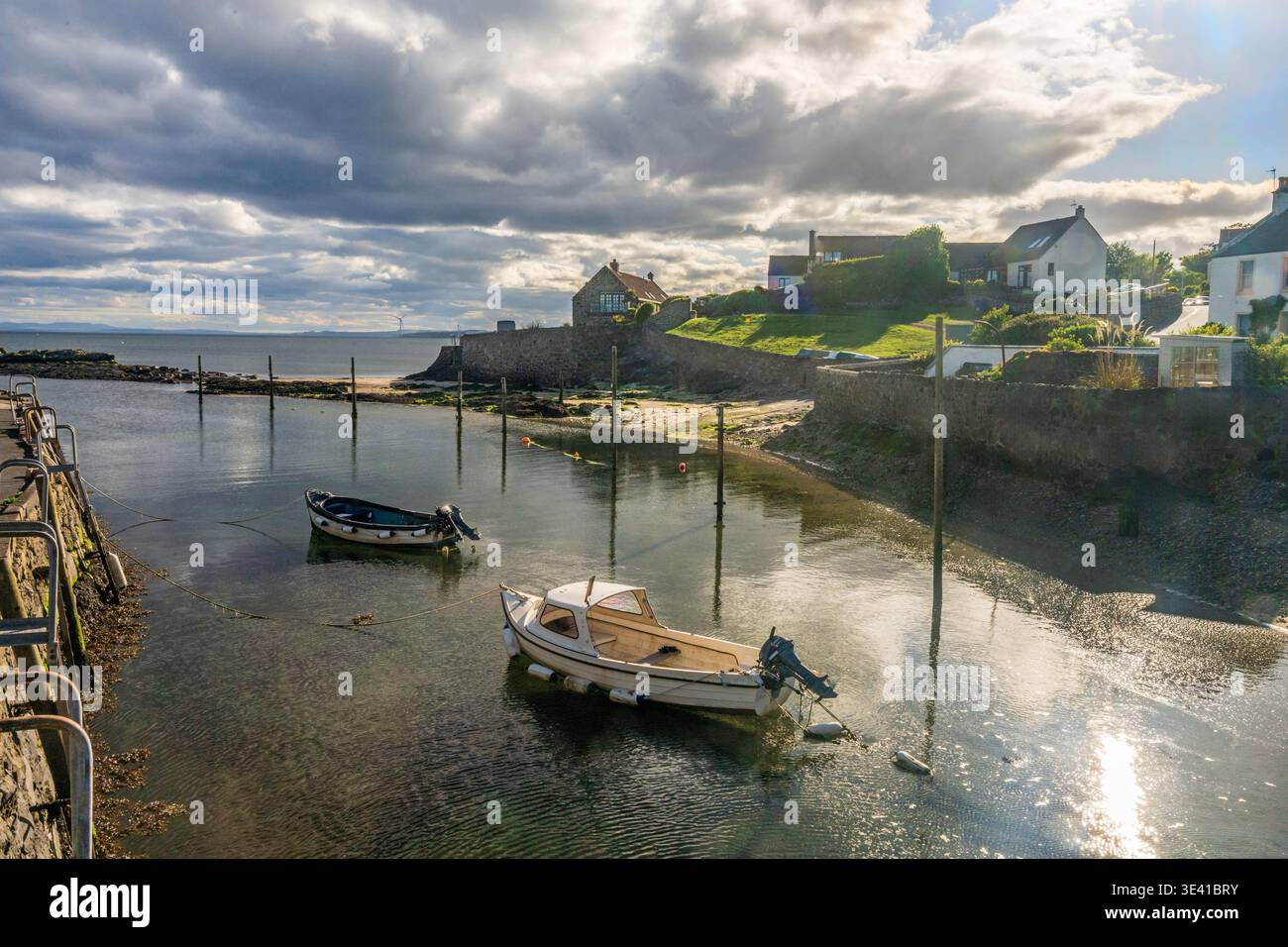 Tranquillo scenario costiero di barche ormeggiate nel porto mareale di Lower largo, Scozia, con pareti di pietra, cottage sul mare, acqua riflettente e Foto Stock
