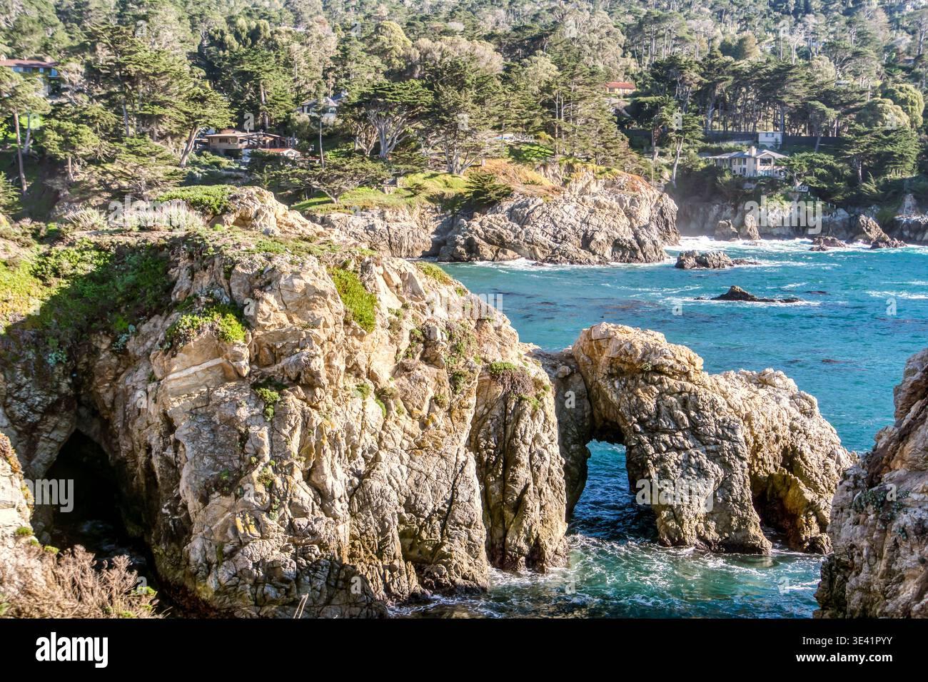 Le scogliere illuminate dal sole incorniciano le onde turchesi dell'oceano. Le rocce rocciose saltano dall'acqua, intemprate dal tempo. Alberi verdi lussureggianti circondano le coste distanti. Luce solare intensa Foto Stock