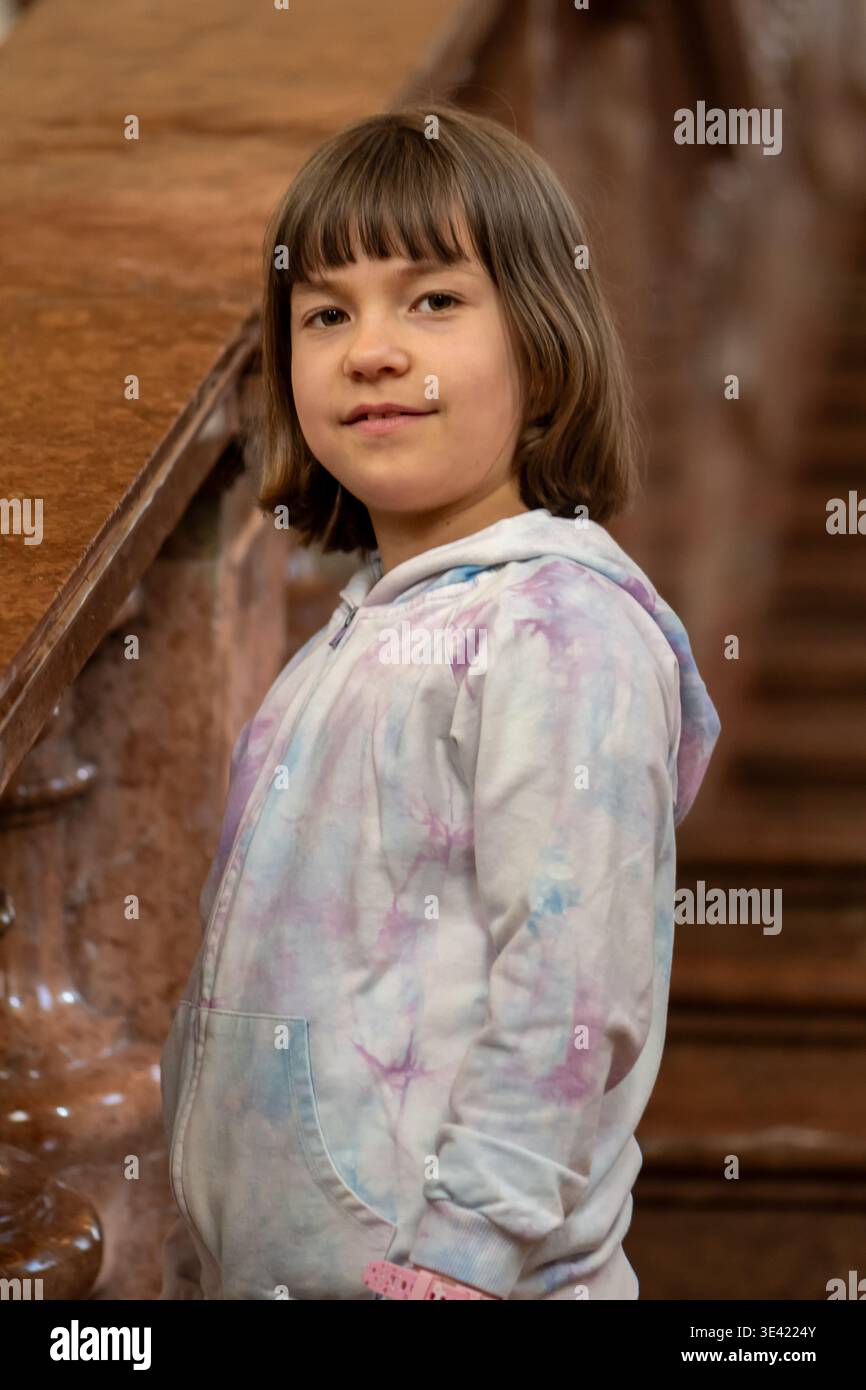 La ragazza di circa 8 anni si trova vicino alla scala e guarda la macchina fotografica. Foto Stock