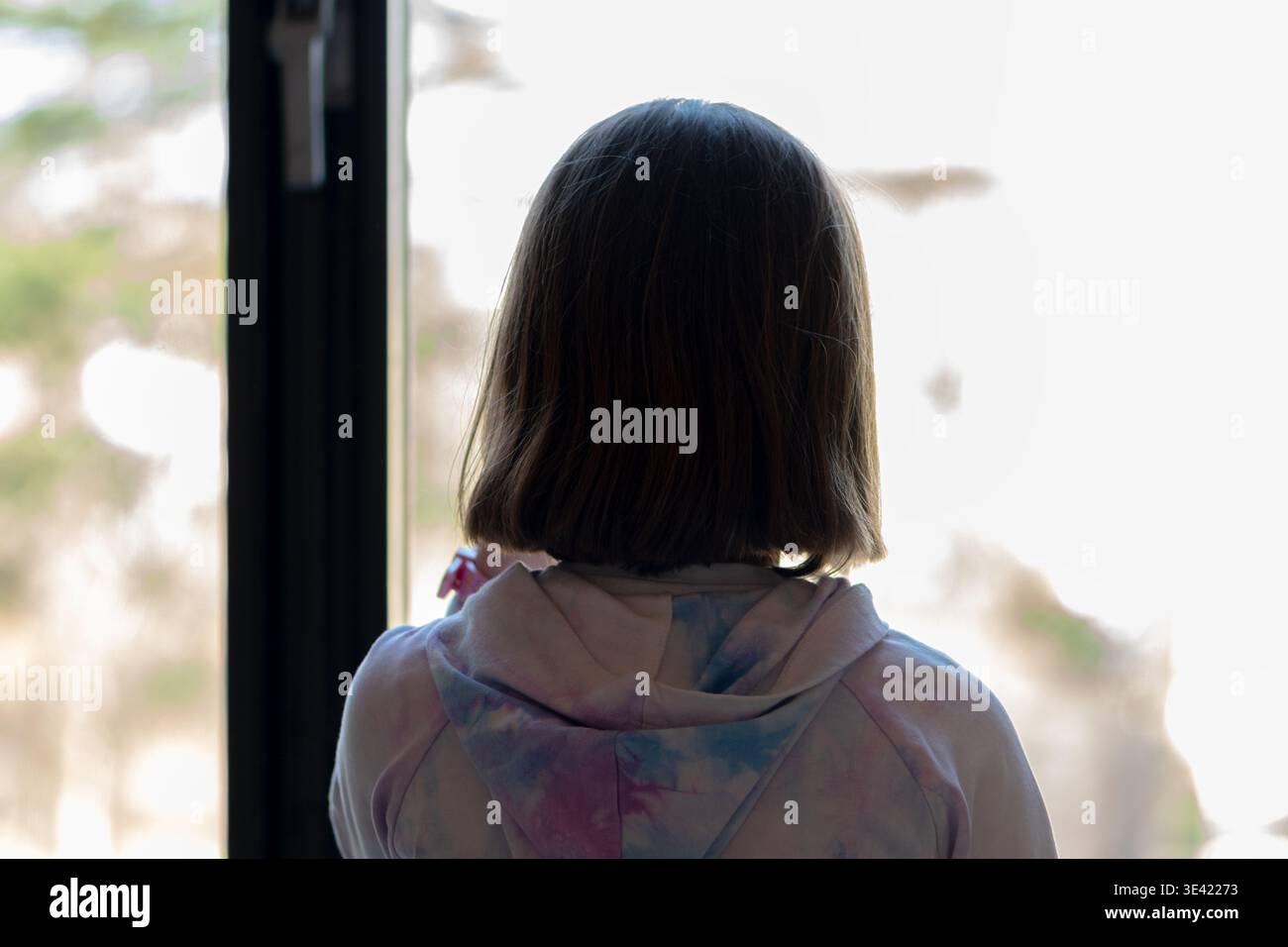 La ragazza di circa 8 anni si trova vicino alla finestra e guarda fuori. Foto Stock