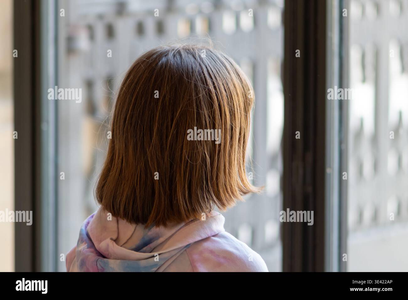 La ragazza di circa 8 anni si trova vicino alla finestra e guarda la città. Foto Stock