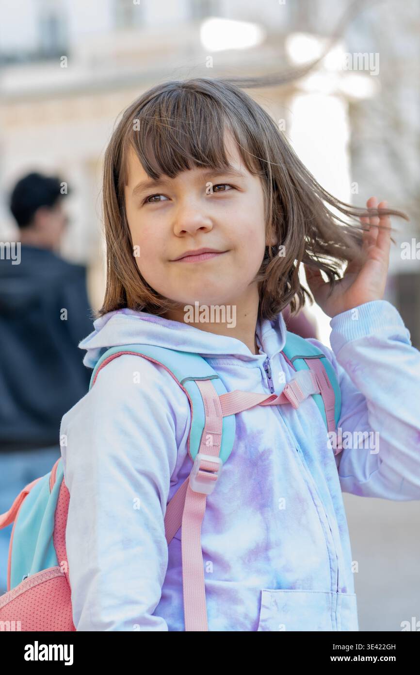 La ragazza di circa 8 anni con lo zaino si tocca i capelli all'aperto. Foto Stock