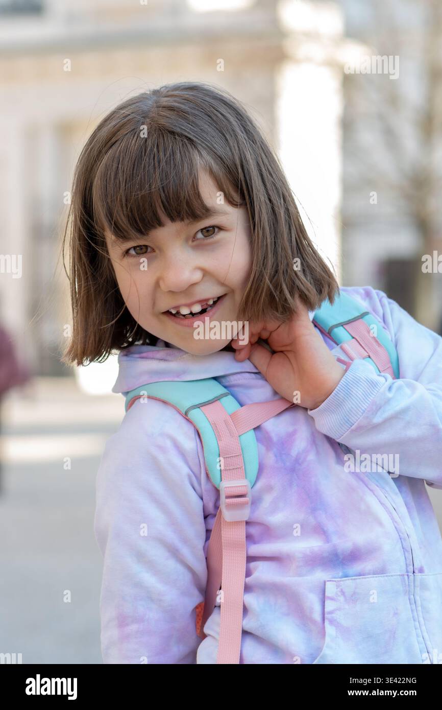 Ragazza di circa 8 anni con lo zaino sorride e posa all'aperto. Foto Stock