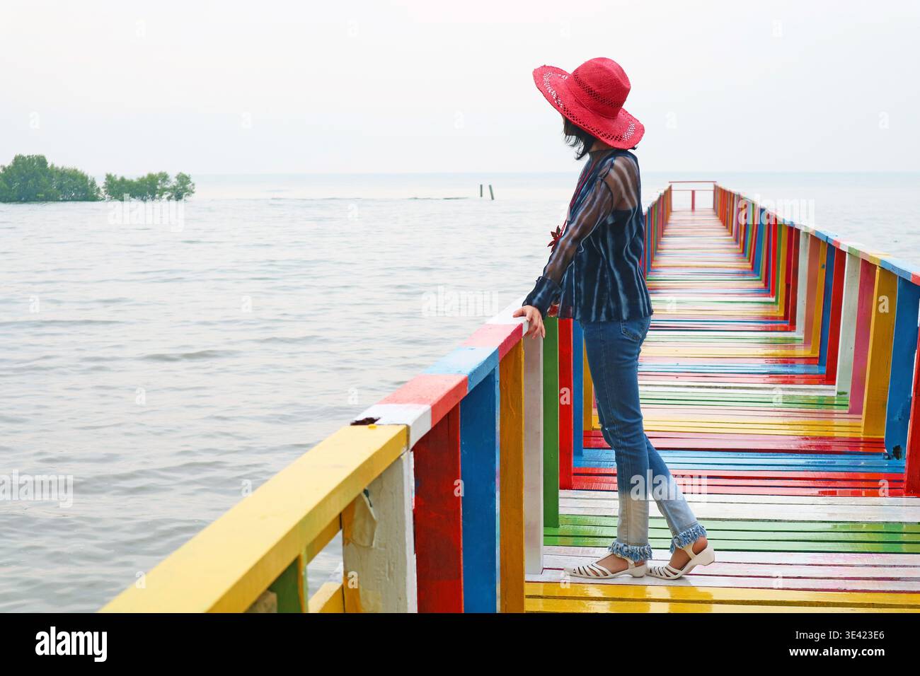 Donna con cappello rosso che guarda il mare dal colorato lungomare di legno Foto Stock