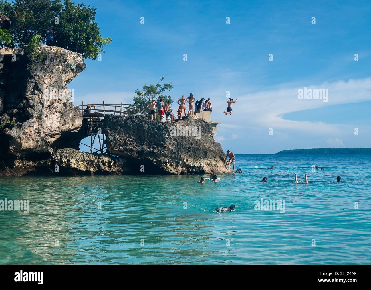 Persone che saltano dalla scogliera e nuotano a Salagdoong Beach, Siquijor, Filippine, con acque cristalline e cieli blu. Foto Stock