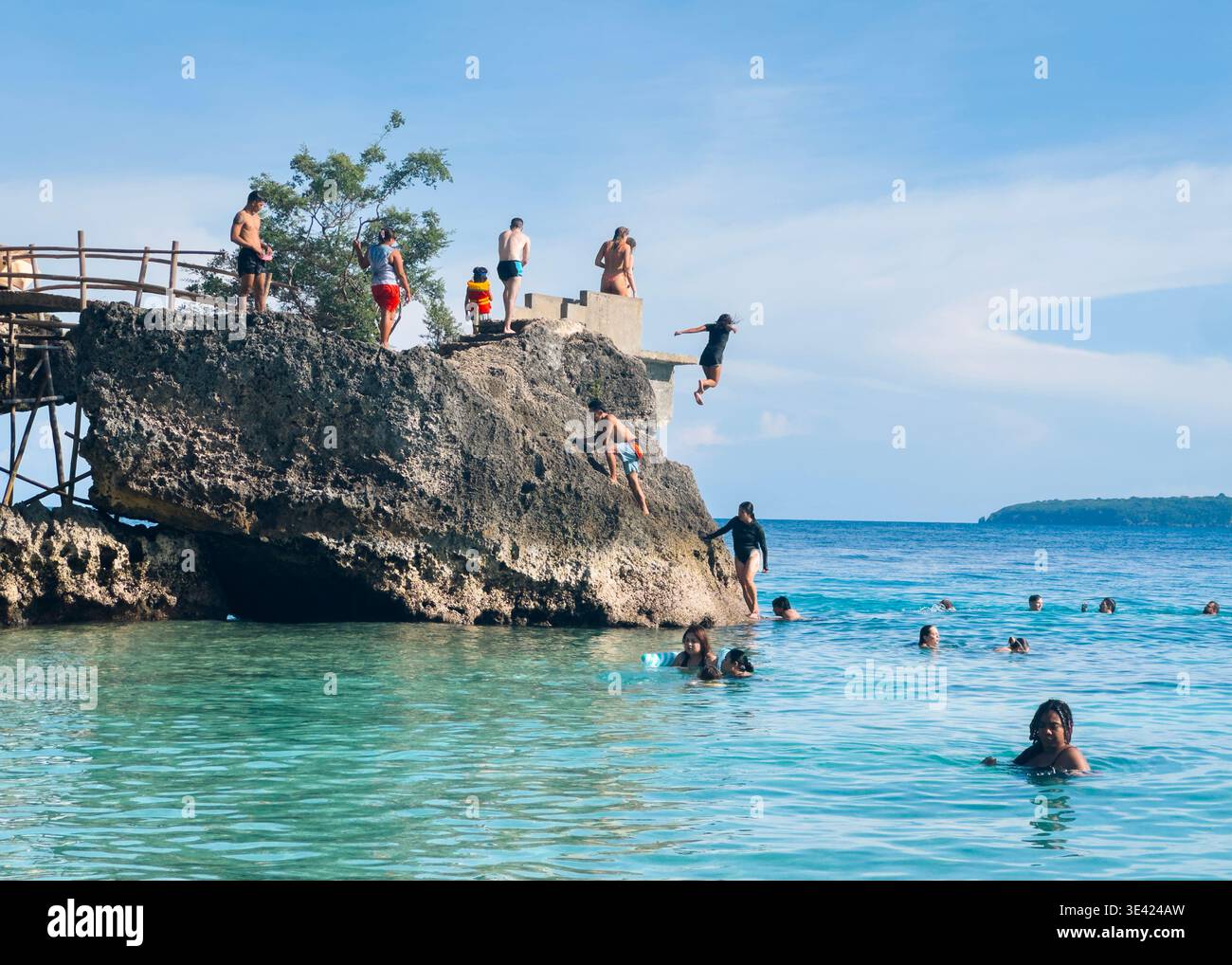 Persone che saltano dalla scogliera e nuotano a Salagdoong Beach, Siquijor, Filippine, con acque cristalline e cieli blu. Foto Stock