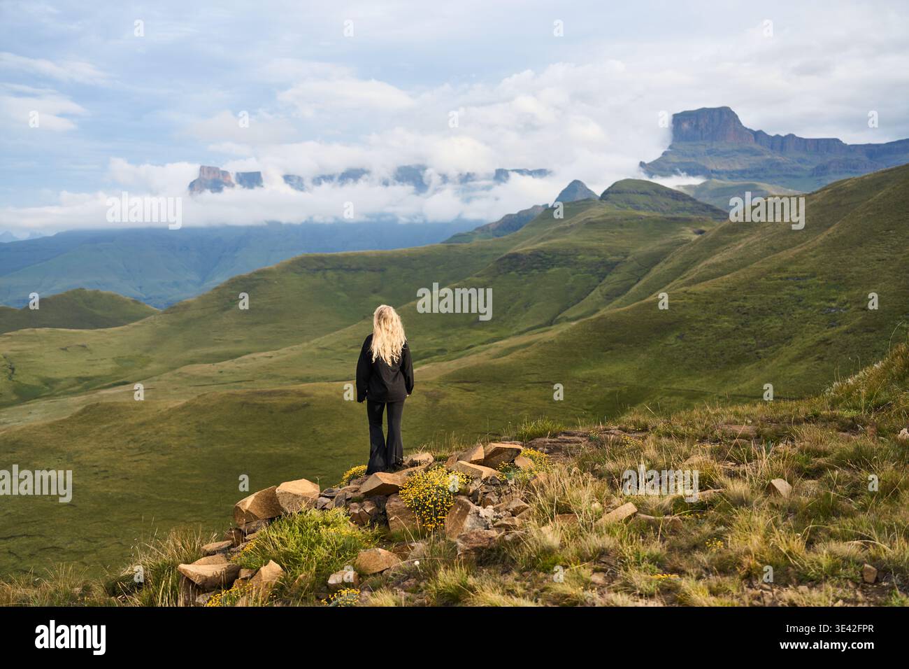 Una donna bionda si erge sul crinale osservando un tranquillo paesaggio naturale Foto Stock