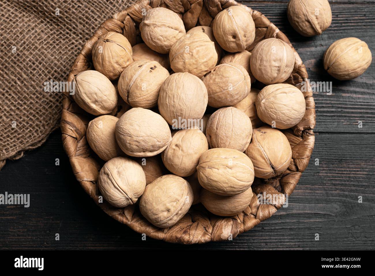 Noci intere in cestello rotondo in vimini su sfondo in legno, vista dall'alto. Cestino di noci. Dieta Paleo e concetto di alimentazione sana. Foto Stock