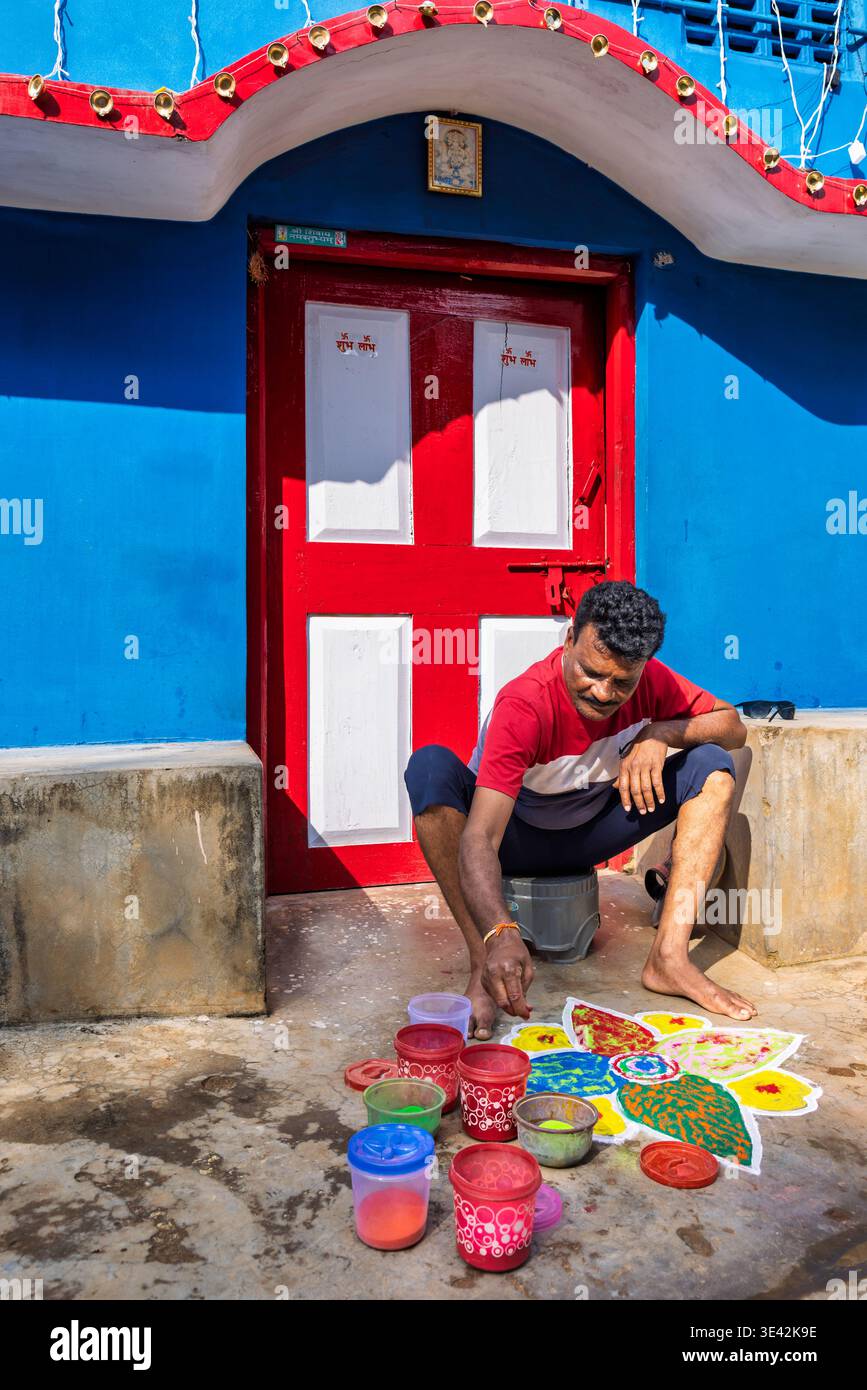 Uomo che fa un Mandala con sabbia colorata di fronte alla sua casa blu, Odisha, India Foto Stock