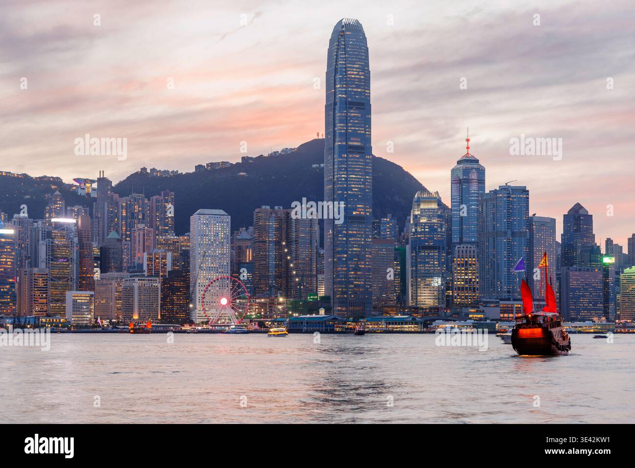 Tradizionale barca in legno con vele rosse sullo skyline di Hong Kong al tramonto, iconica scena urbana Foto Stock