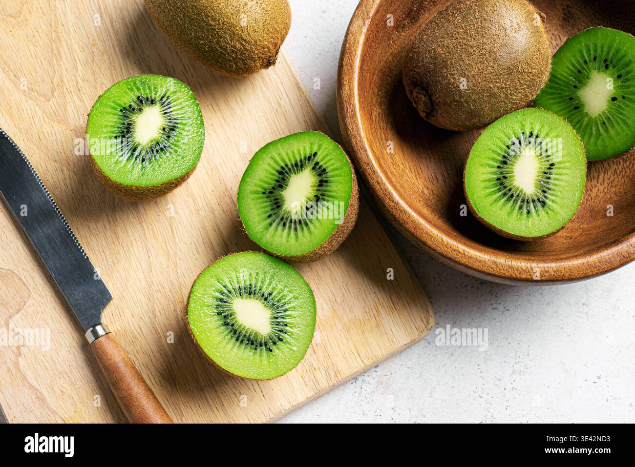 Frutta kiwi in una ciotola di legno. Frutta intera e mezzo pezzetti di kiwi verde da vicino. Kiwi maturo fresco. Alimentazione sana organica. Foto Stock