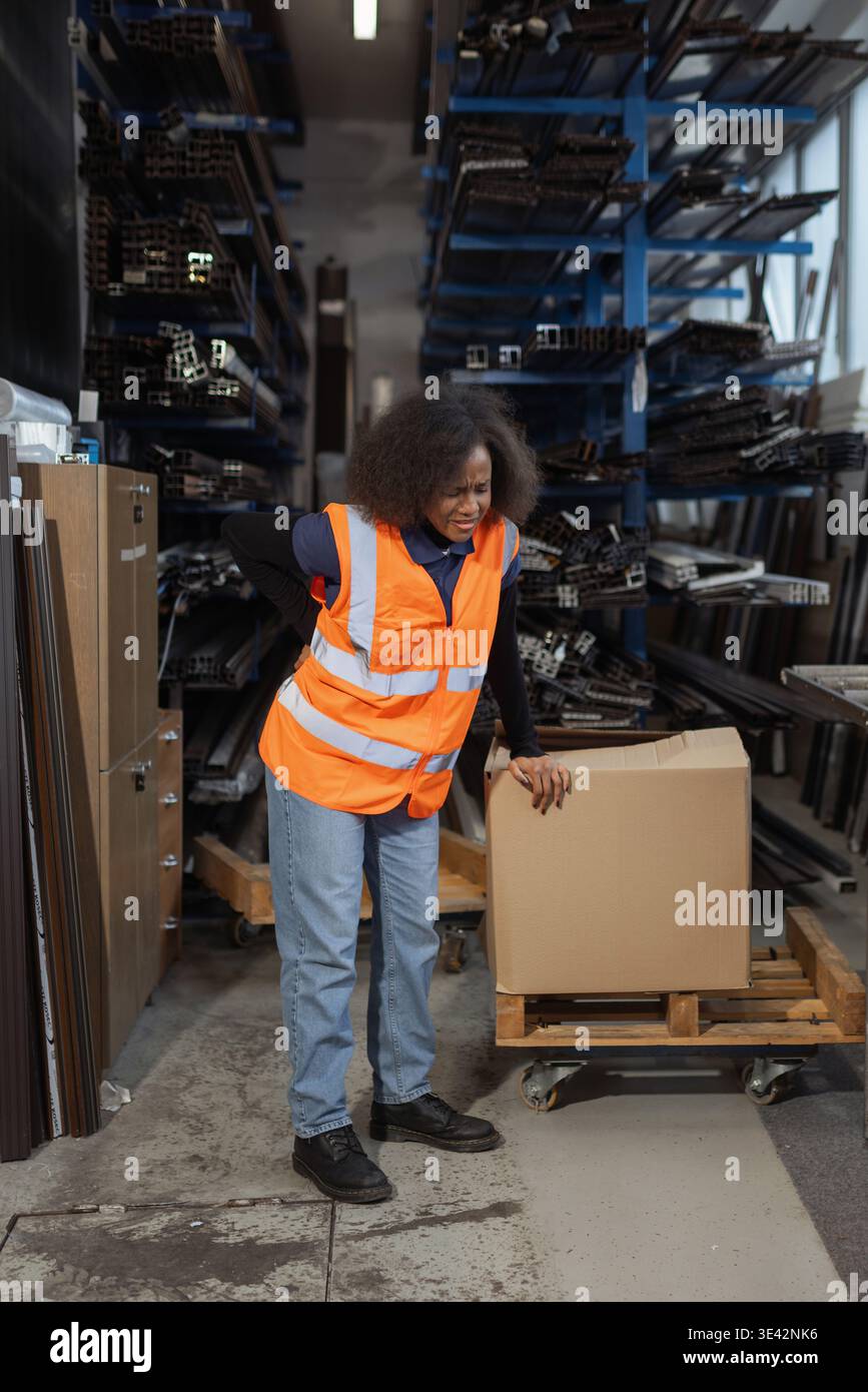 Donna addetto alla logistica e al magazzino che soffre di mal di schiena dopo la movimentazione manuale, il sollevamento e il trasporto di pesanti scatole di cartone. Foto Stock