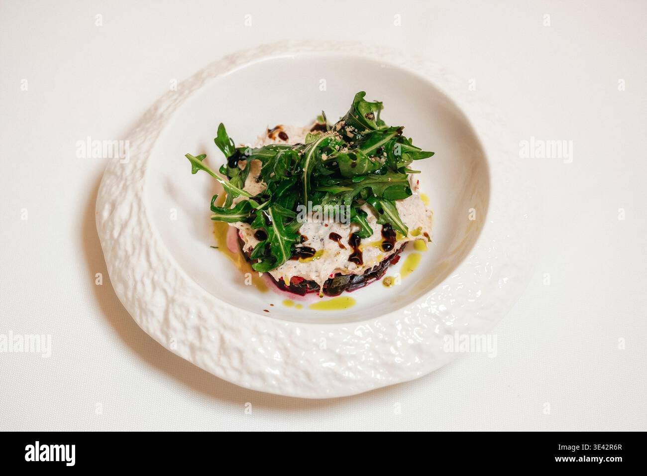 Insalata di rucola con burrata, gocciolatoio di aceto balsamico, olio d'oliva, peperoncino crepato su bianco testurizzato Foto Stock