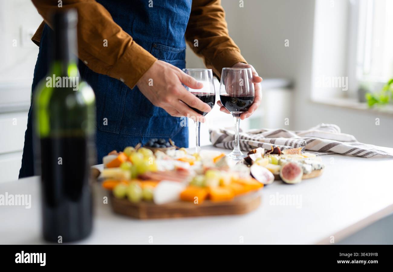 L'uomo in grembiule prepara bicchieri da vino e Un Cheese Board per Una cena romantica per due Foto Stock