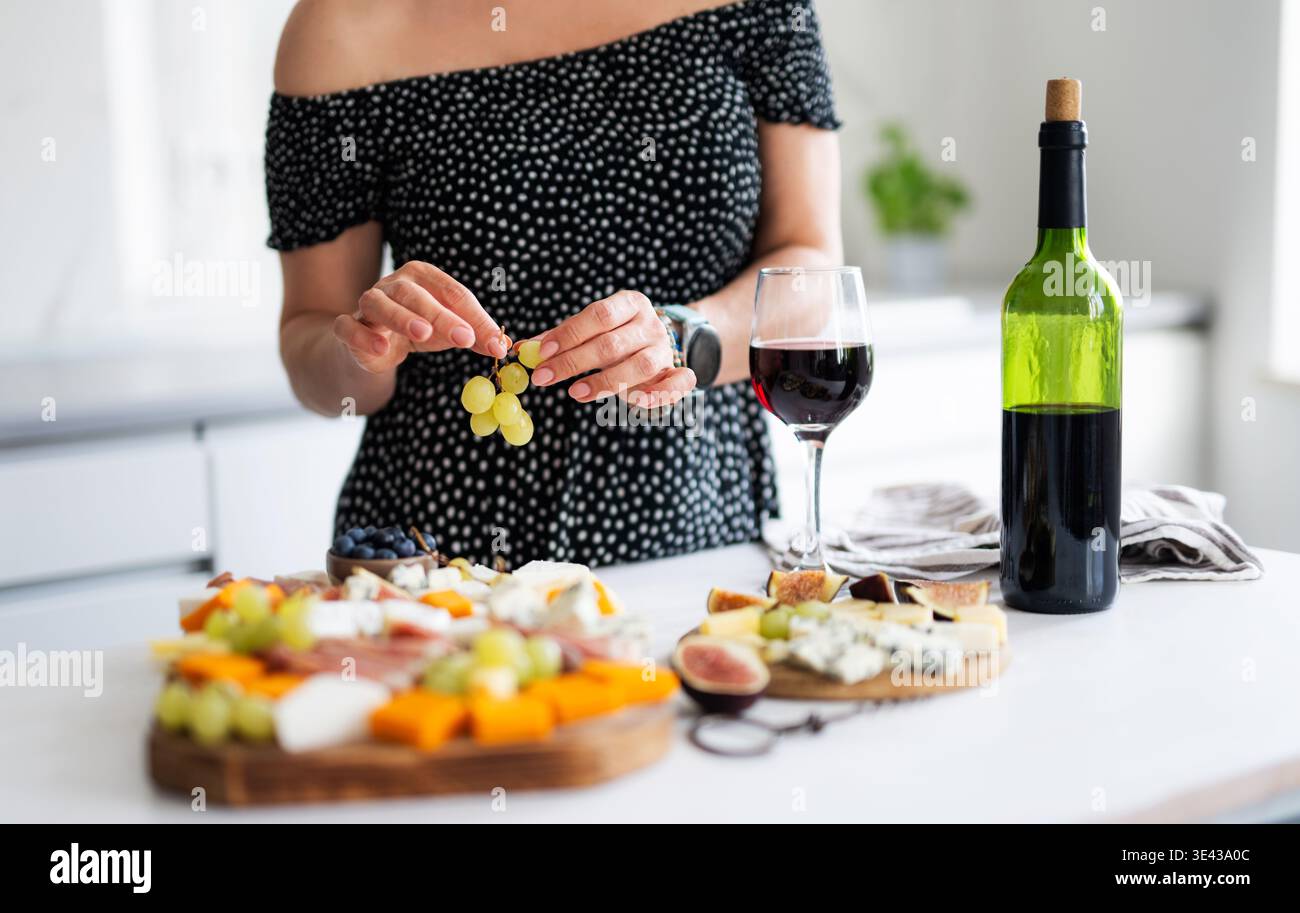 Ragazza che beve Un bicchiere di vino in cucina con un piatto di formaggi dopo Una dura giornata Foto Stock