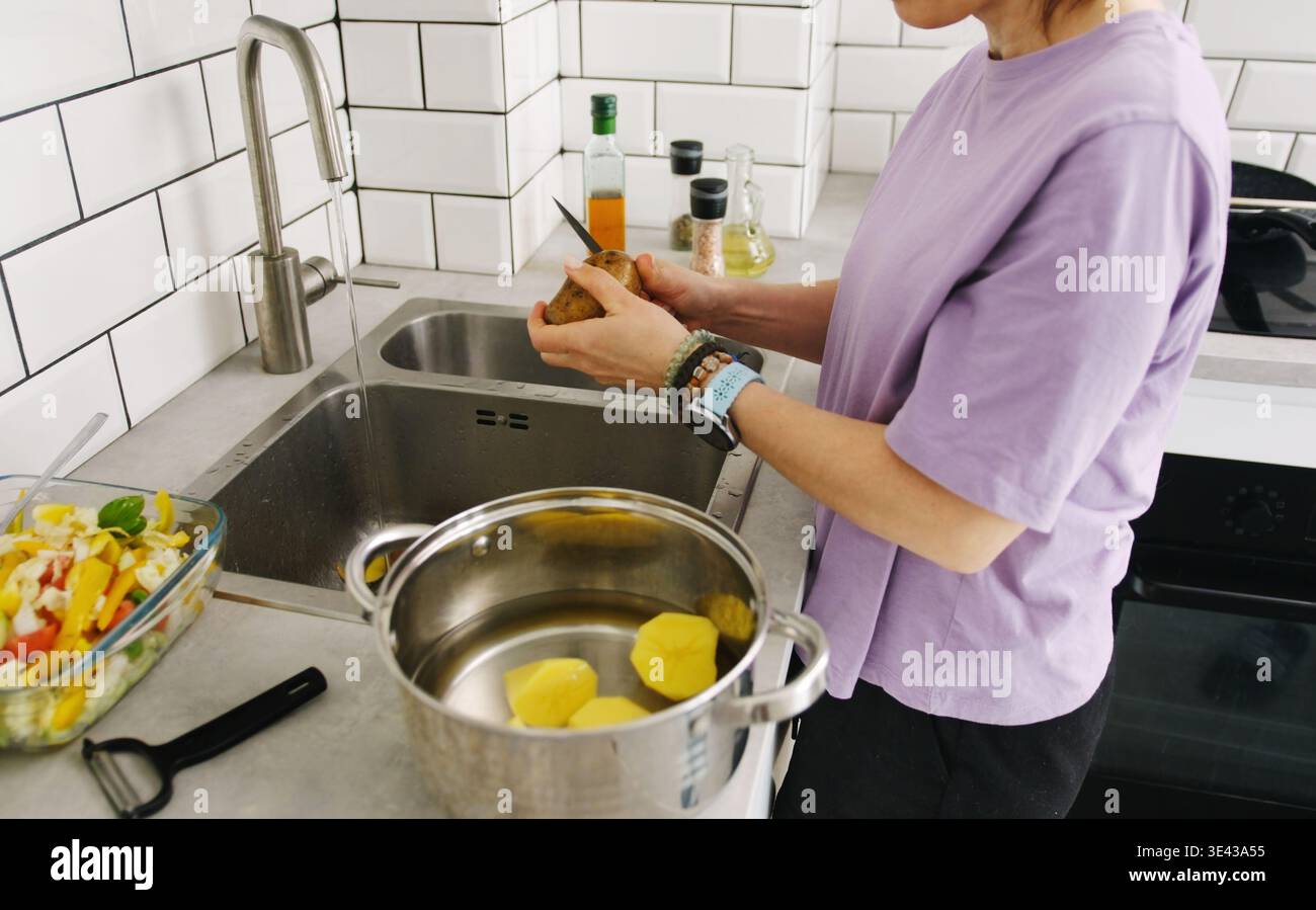 Donna che sbuccia Una patata in cucina e la taglia in Una pentola Foto Stock