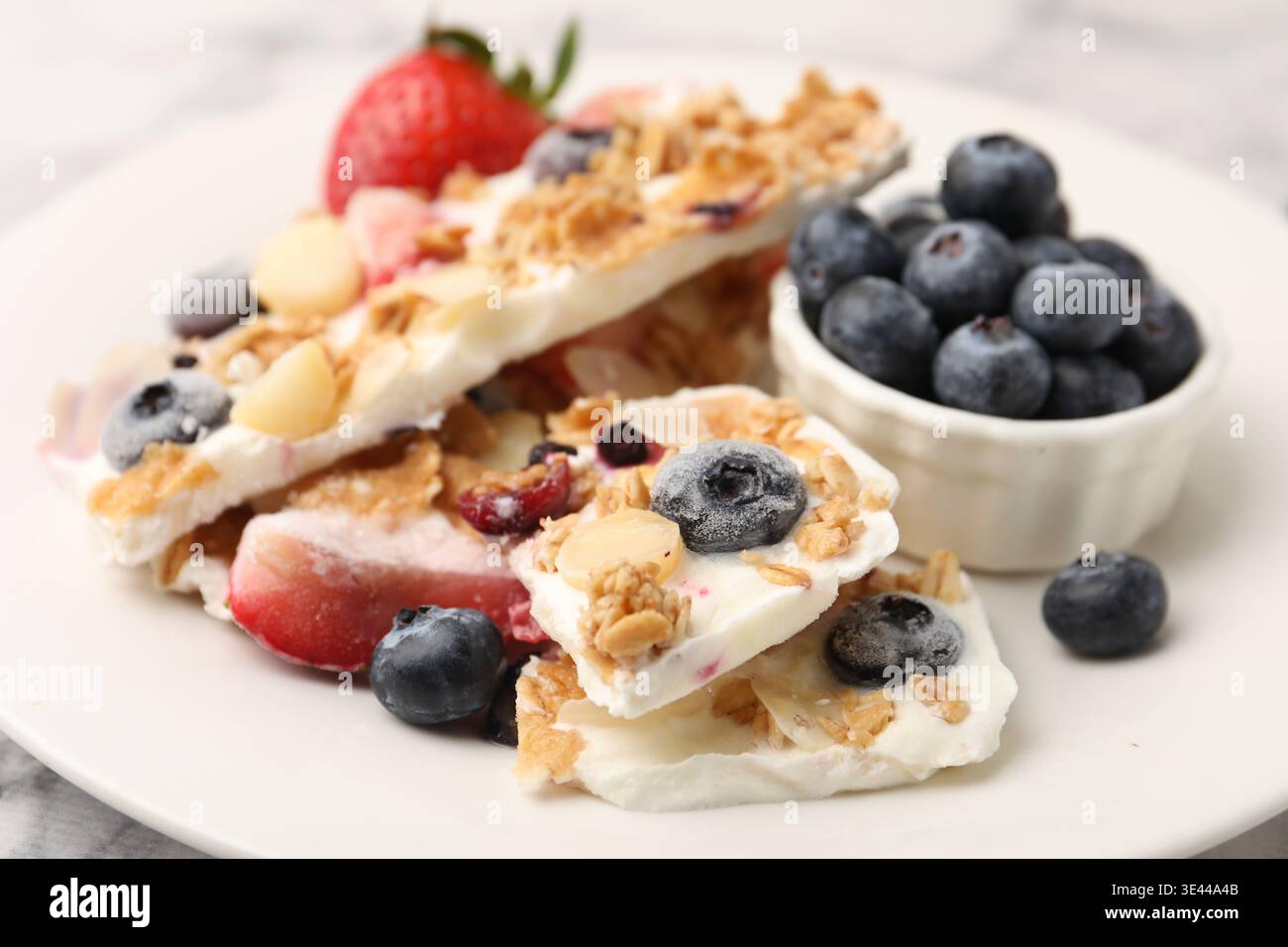 Pezzi di gustosa corteccia di yogurt con frutti di bosco, scaglie di mandorle e muesli sul tavolo, primo piano Foto Stock