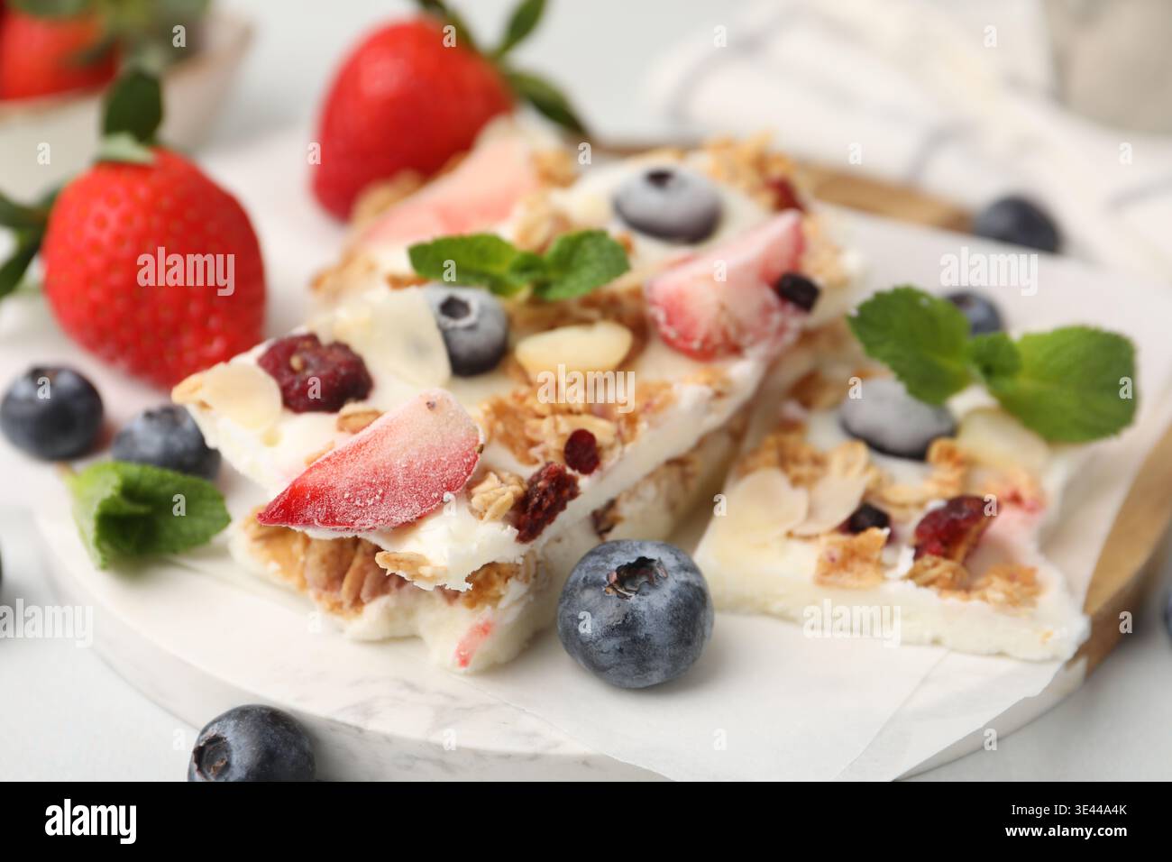 Pezzi di gustosa corteccia di yogurt con frutti di bosco, muesli e menta sul tavolo leggero, primo piano Foto Stock
