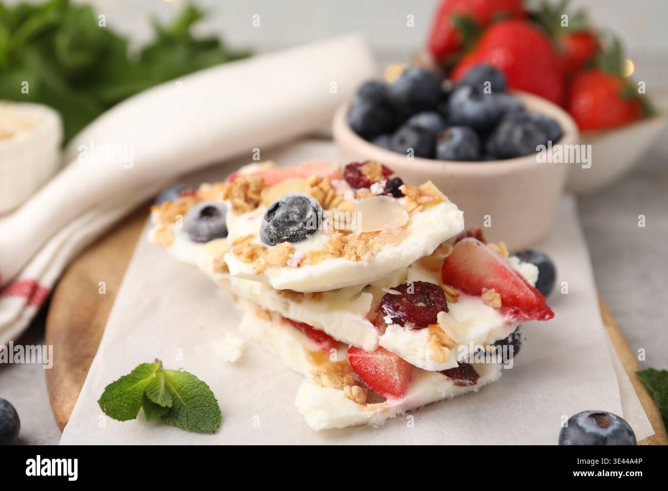 Pezzi di gustosa corteccia di yogurt con frutti di bosco, muesli e menta sul tavolo grigio, primo piano Foto Stock